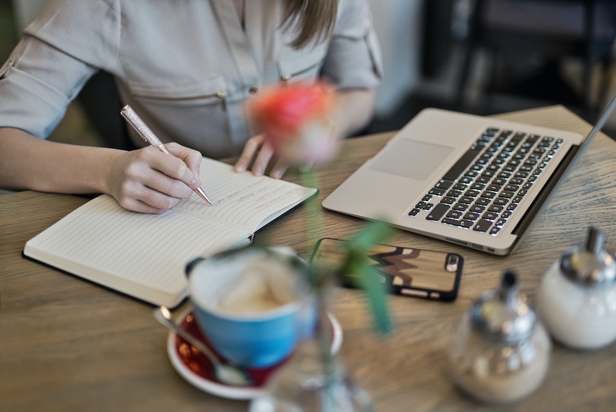 person writing on notebook beside a laptop computer